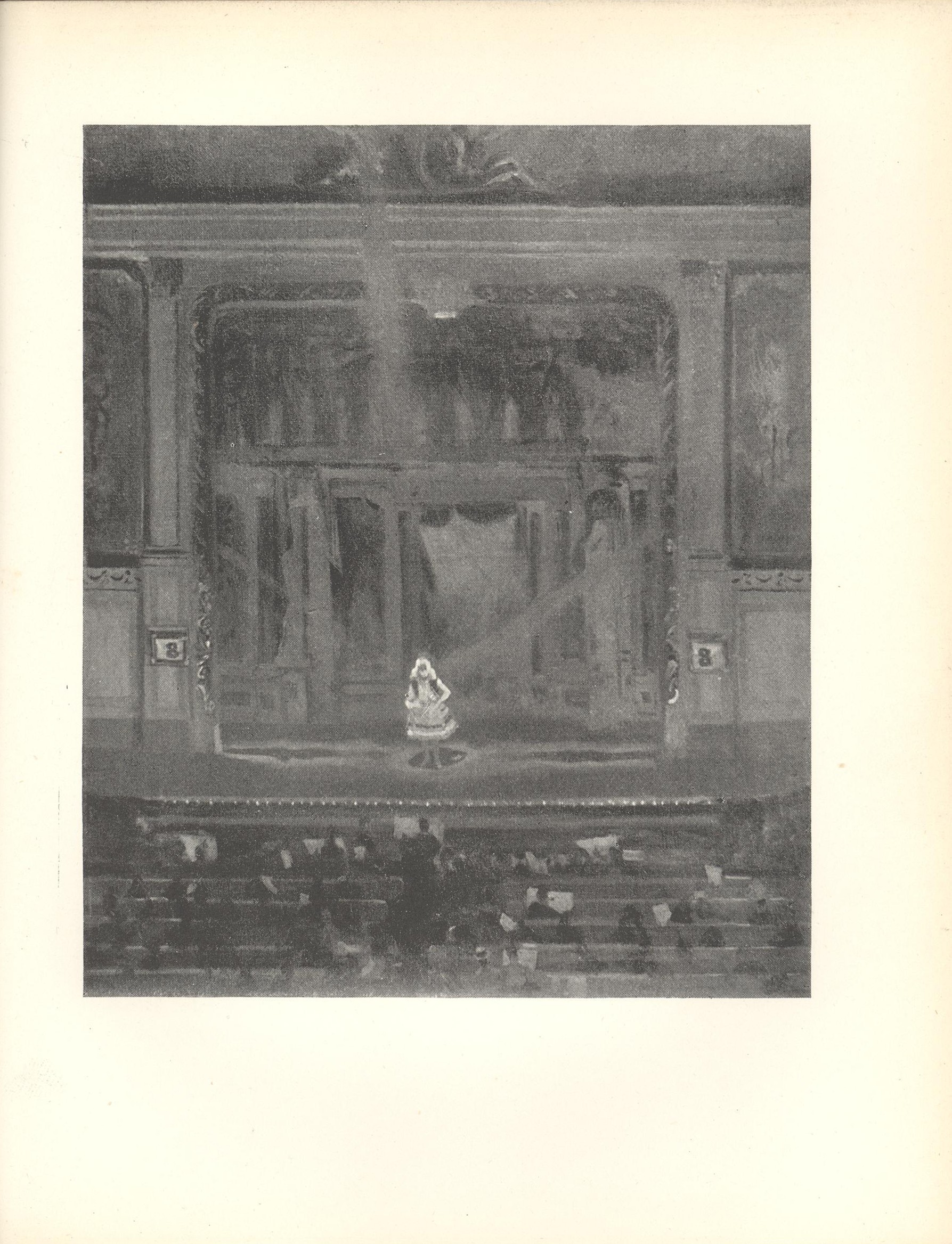 Image is of a music hall viewed from the back of the theatre. The stage divides the frame into three sections The central and largest section is the performance area where a small blonde woman wearing a short white dress is standing on a proscenium stage The theatrical facade behind the woman contains many curtains and lights The upper section at the extreme top of the image is of some moulding over centre stage The lower section of the image is comprised of several rows of audience members the orchestra pit and the conductor The image is vertically displayed