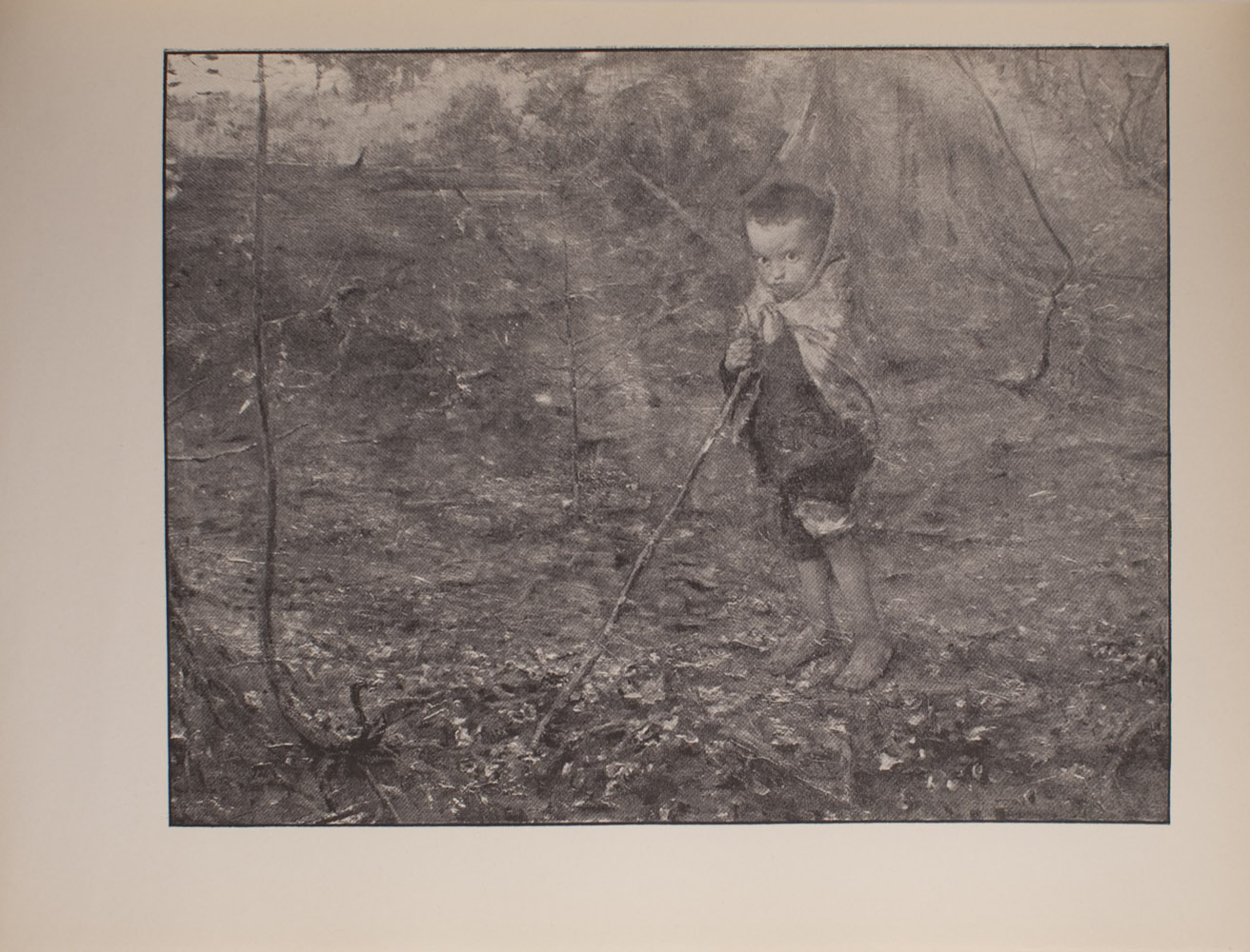 The image is of a young boy in a wooded area The boy stands barefoot holding a long stick that extends diagonally to the left He is wearing pants which are rolled up to his knees and appears to have a scarf or blanket wrapped around his shoulders and the back of his head The boy faces the viewer The image is horizontally displayed
