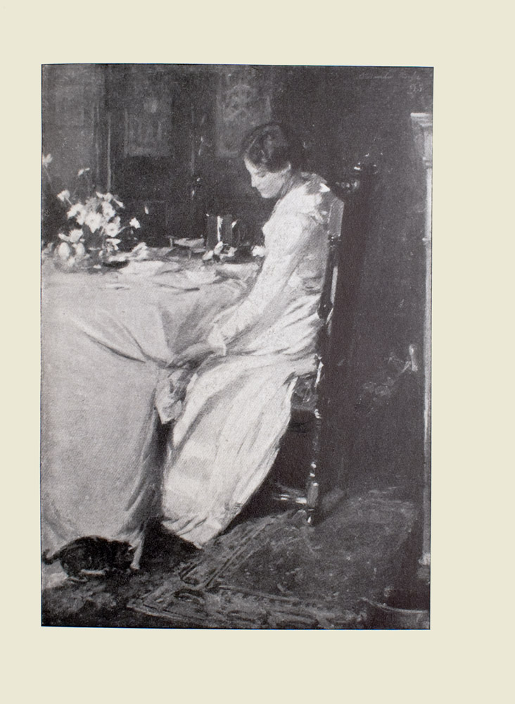 Image is of a woman sitting at a table in a dining room She is shown in profile, facing the left Her body divides the image in half vertically The woman is wearing a long white dress that reaches the floor Her dark hair is tied back She is sitting in a tall dark chair that is only slightly shorter than her frame Her left hand is reaching down towards the ground where a small dark cat is sniffing the bottom of the white tablecloth Under the chair is a detailed Persian rug On the table are place settings and a vase of white daisies Behind the woman is the white mantel of a fireplace In the bottom right hand corner there is a brass pot In the background the faint outline of cabinets can be seen The image is vertically displayed
