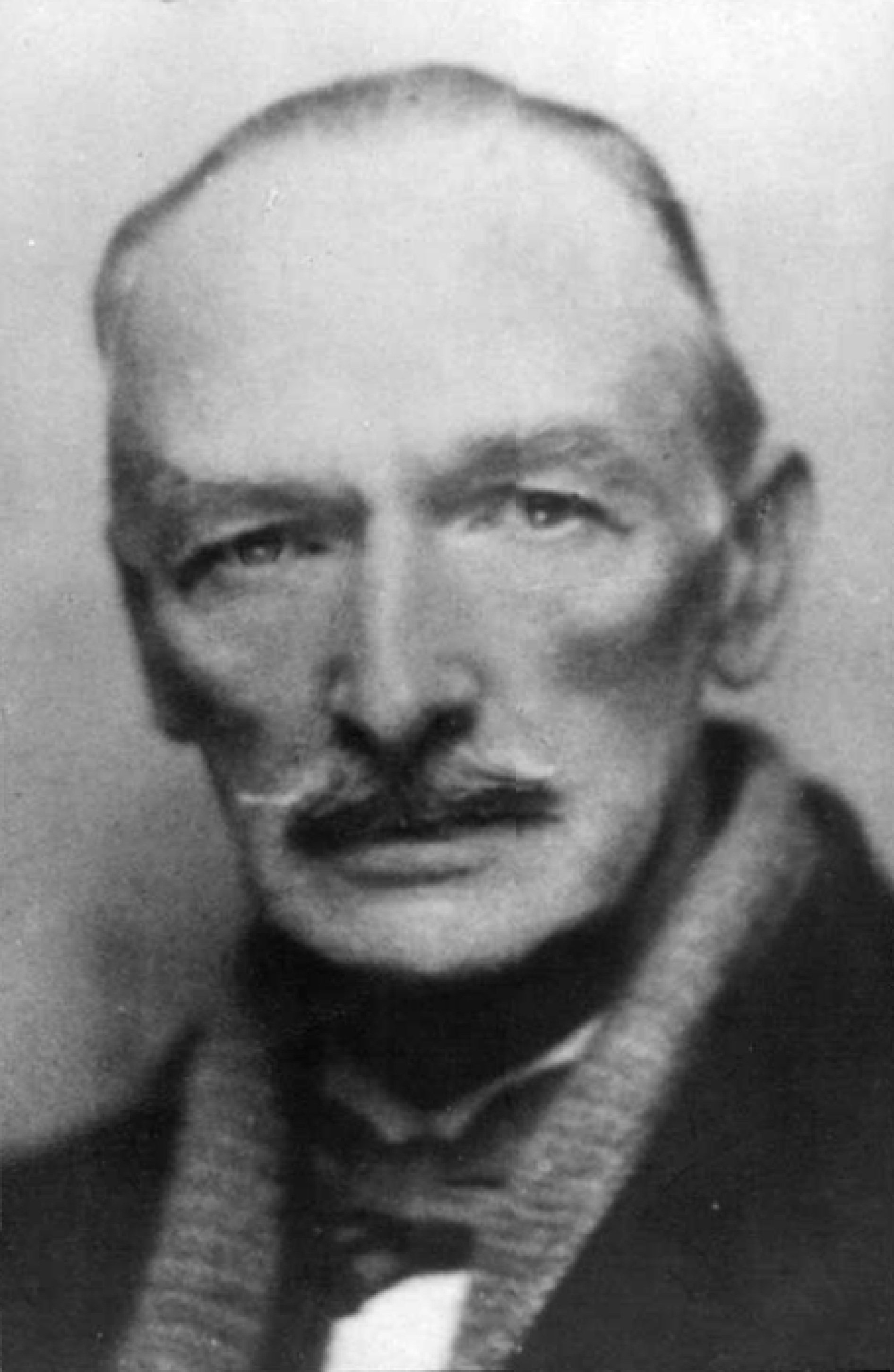 The photograph shows Wilson almost full faced. He sports a moustache that covers his upper lip. He is wearing a scarf and coat and a bowtie is visible. The photograph is soft focused.
