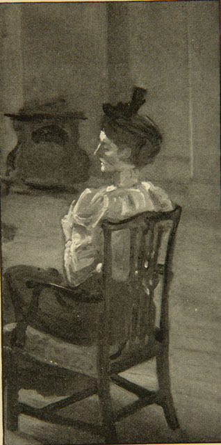 Black-and-white image of a woman, possibly Ella D’Arcy, sitting in a chair with her back to the viewer. The front of the chair faces the left of the frame. The woman’s eyes are cast down, and her head faces away from the viewer to the left. She is wearing a white long-sleeve shirt and dark –coloured skirt, with a black headpiece. There is a fireplace in the background.